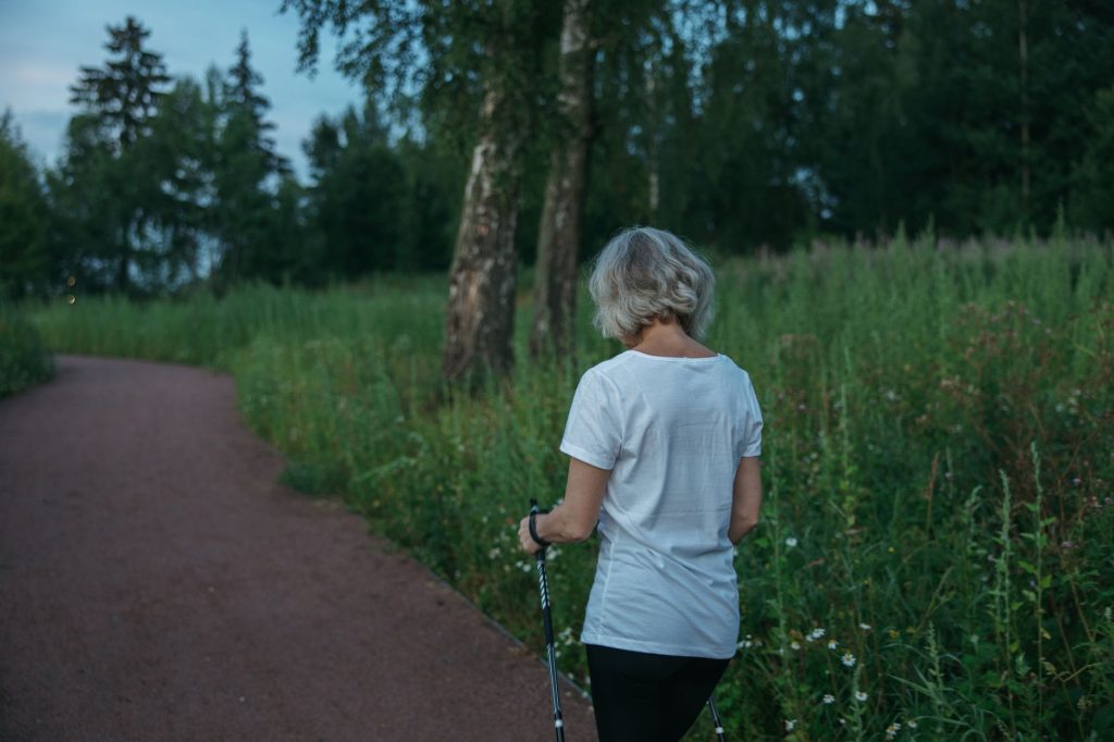 An older woman Nordic walking with poles on a green park trail